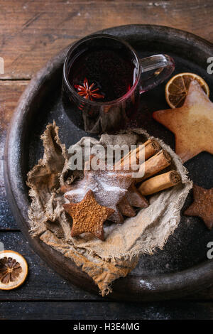 Tasse en verre de vin chaud rouge chaud d'épices, sablés sucre star shape, l'anis et la cannelle en poudre dans le bac d'argile sombre sur w Banque D'Images