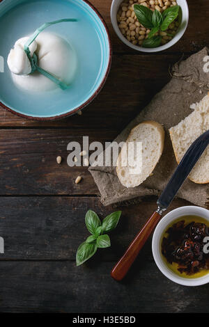 Bol Turquoise ensemble lié à la saumure de burrata fromage italien servi avec des tranches de pain, les noix de pin, le basilic et les tomates séchées dans l' Banque D'Images