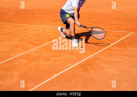 Joueur de tennis masculin en action sur la terre battue sur une journée ensoleillée Banque D'Images