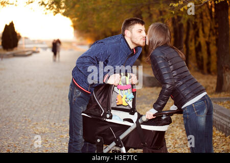 Heureux parents kiss pour une promenade près de la poussette Banque D'Images