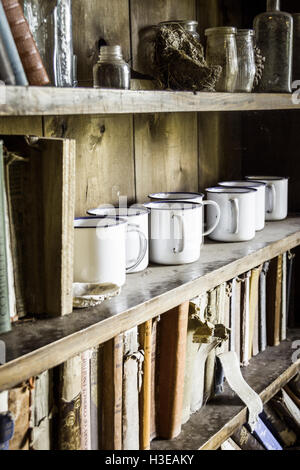 Droit aux teintes chaleureuses de l'émail blanc des tasses, des pots de verre et les livres sur des étagères dans une vieille bibliothèque ou une commode Banque D'Images