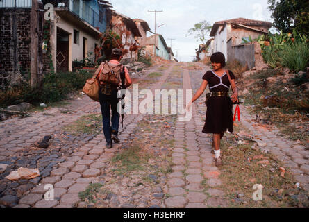 TENANCINGO, EL SALVADOR, mars 1984 : - dans le FPL Les zones de contrôle. Une jeune femme guérillero sourit à un ami comme elle passe lui dans la rue en ruine de Tenancingo. Banque D'Images