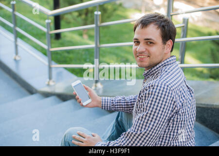 Jeune homme assis sur un escalier tenant un téléphone intelligent. Banque D'Images