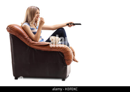 Jeune femme assise sur un fauteuil d'un changement de chaîne sur la TV et eating popcorn isolé sur fond blanc Banque D'Images