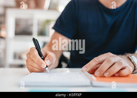 Close up de mains d'un jeune homme qui écrit dans un journal personnel de bureau. L'accent sur la plume de l'homme d'affaires. Banque D'Images