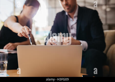 Tiré de deux businesspeople sitting ensemble et travailler sur ordinateur portable. Réunion des cadres dans un hall de l'office. Woman pointing at lapto Banque D'Images