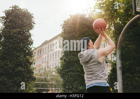 Image d'un joueur de streetball jouant sur la cour extérieure. Jeune homme athlétique en tenant le tir en basket-ball. Banque D'Images