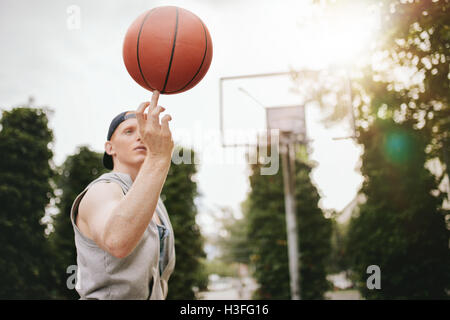 Jeune homme basket-ball d'équilibrage sur le doigt sur une cour. Joueur de Streetball de faire tourner la balle. Se concentrer sur le basket-ball. Banque D'Images