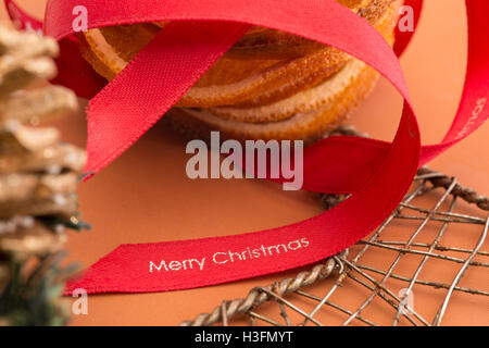 Bande de ruban rouge avec le texte 'Merry Christmas' imprimé sur et par une pile de tranches de fruits d'orange séchée décorative et un fil Banque D'Images