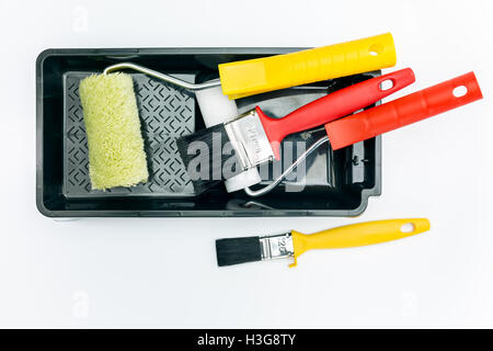 Rouleaux à peinture et pinceaux sur bac noir sur fond blanc Banque D'Images