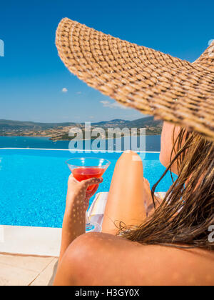 Femme tenant un cocktail rafraîchissant au bord de la piscine à débordement en Grèce Banque D'Images