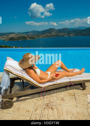 Femme avec un cocktail rafraîchissant au bord de la piscine à débordement en Grèce Banque D'Images