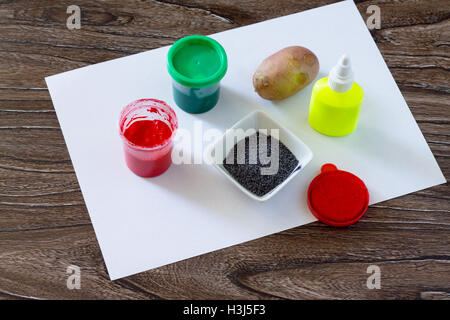 L'enfant fait de dessin sur le papier à l'aide de la pommes de terre et d'impression les doigts. Peinture, Colle, papier et les pommes de terre sur une table en bois. Chi Banque D'Images