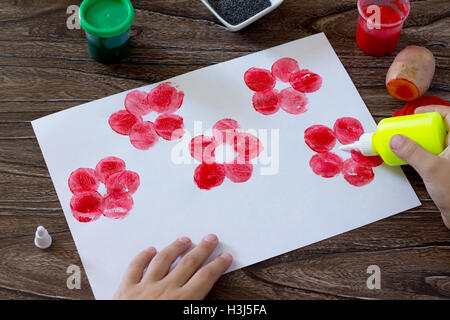 Dessin sur papier coquelicots, appliquez de la colle dans l'enfant des coquelicots en papier. Peinture, Colle, papier et les pommes de terre sur une table en bois. Un des enfants Banque D'Images