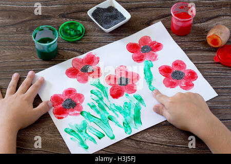 Dessin sur papier coquelicots, les doigts de l'enfant attire l'herbe. Peinture, Colle, papier et les pommes de terre sur une table en bois. Projet d'art pour enfants, Banque D'Images