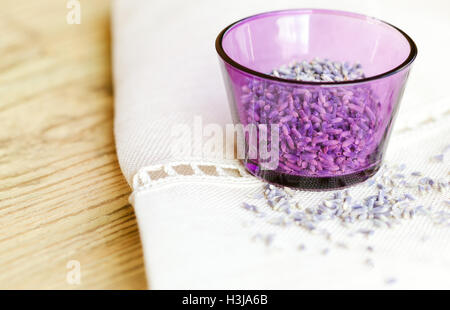 Les fleurs de lavande séchées dans un verre violet sur le tissu et le bois. Lavandula angustifolia avec fleurs mauve pâle. Herbes culinaires. Banque D'Images