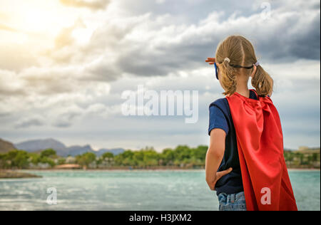 Super héros enfant regardant sur le coucher du soleil. Banque D'Images