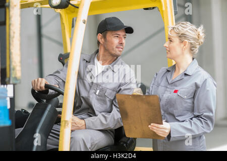 Les superviseurs d'usine avec presse-papiers parlant à conducteur de chariot élévateur à l'usine d'emballage Banque D'Images