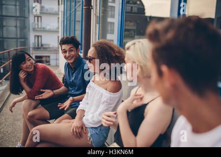 Groupe multiracial d'amis assis sur un balcon. Les jeunes de détente en plein air en terrasse. Banque D'Images