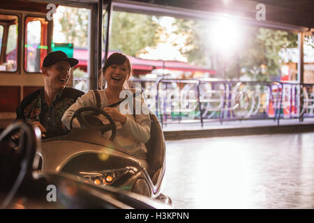 Happy young man and woman driving auto tamponneuse au parc des expositions. Jeune couple riding auto tamponneuse au parc d'amusement. Banque D'Images