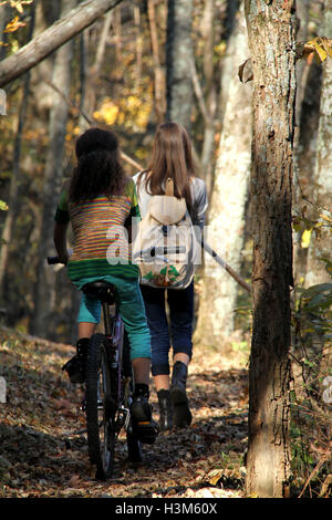 Deux filles vélo et randonnées sur sentier forestier à l'automne Banque D'Images