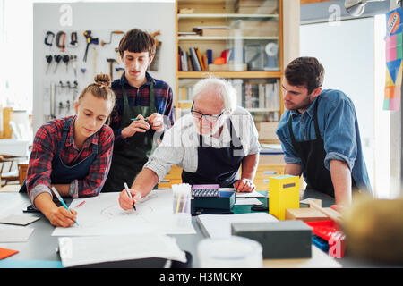 Senior male artisan remue-méninges avec groupe de jeunes hommes et femmes dans l'atelier des arts du livre Banque D'Images