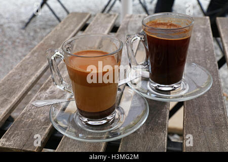 Deux fraîchement moulu turc terrain naturel café, noir et au lait, en plein verre transparent avec tasses et soucoupe metal Banque D'Images