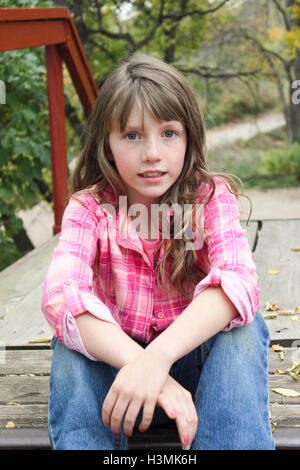 Petite fille assise sur l'escalier en bois coloré en chemise à carreaux roses et posant pour l'appareil photo Banque D'Images