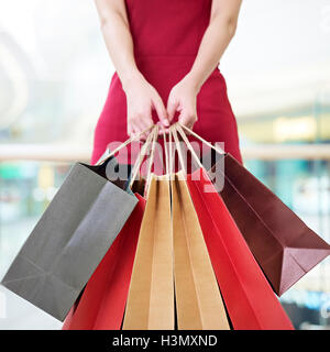 Jeune femme female shopper debout avec des sacs de papier coloré en mains en centre commercial ou grand magasin, se concentrer sur les sacs en papier Banque D'Images