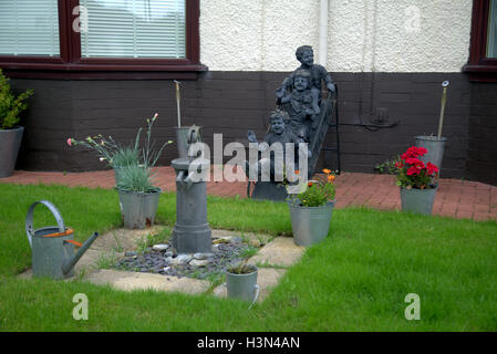 Ornements de jardin dans un petit jardin de banlieue enfants seaux pompe sur une pelouse avec des fleurs Banque D'Images