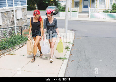 Deux amies aux cheveux roses walking on sidewalk carrying shopping bags Banque D'Images