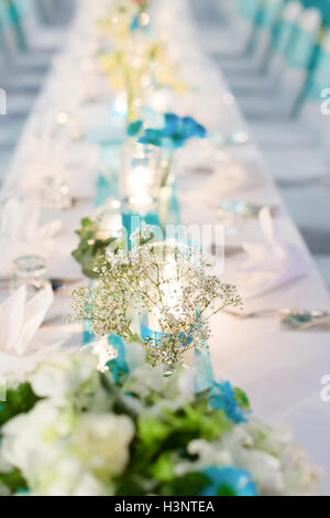 Dîner romantique, configuration thème blanc et bleu décoré de la lumière des bougies, des lanternes et des fleurs. Focus sélectif. Banque D'Images