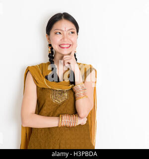 Portrait of happy young Indian Chinese girl en punjabi traditionnelle robe est pensée, debout sur plain white backgrou Banque D'Images