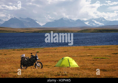 Moto enduro voyageur seul dynamique paysage coloré tente highland shore steppe de blue lake couvertes de glace neige mont élevé Banque D'Images