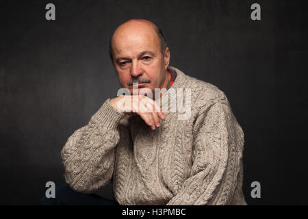 Un homme âgé est assis et regarde pensivement, méditant problème ou question complexe en pull. Banque D'Images