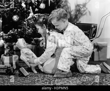 1940 Garçon Fille FRÈRE SŒUR REGARDANT GOLDEN CHRISTMAS BALLS GIRL HOLDING BABY DOLL Banque D'Images