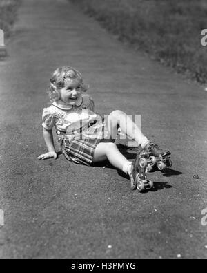 1940 FILLE TOMBER ASSIS SUR UN TROTTOIR portant des patins à roulettes en métal Banque D'Images