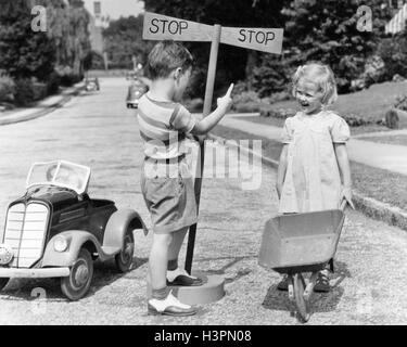 Années 1930 Années 1940 Garçon jouant de la circulation pointant à l'arrêt l'arrêt de fille avec Brouette Banque D'Images