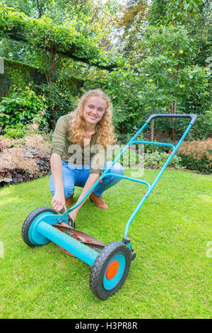 Young caucasian woman reparing tondeuse sur l'herbe verte Banque D'Images