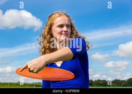 Young caucasian woman holding orange extérieur frisbee contre le ciel bleu Banque D'Images