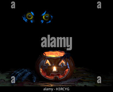 Décoration de citrouilles rougeoyant, skeleton hand, spider et owl eyes en fond sombre Banque D'Images
