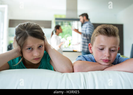 Les enfants triste appuyée sur un canapé, tandis que parents se disputer en arrière-plan Banque D'Images