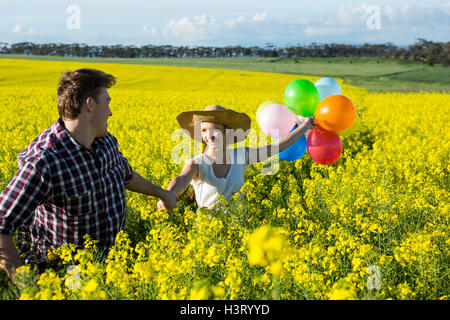 Couple holding colorful balloons dans champ de moutarde Banque D'Images