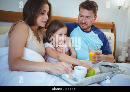 Les parents assis sur le lit avec sa fille et le petit-déjeuner Banque D'Images