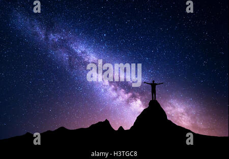 Voie lactée. Silhouette d'un homme debout avec les armes sur le sommet de la montagne. De hautes roches, sommet de montagne. Belle galaxie. Banque D'Images