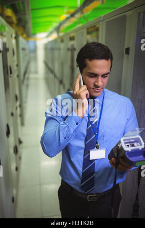 Techniciens talking on mobile phone pendant l'analyse de server Banque D'Images