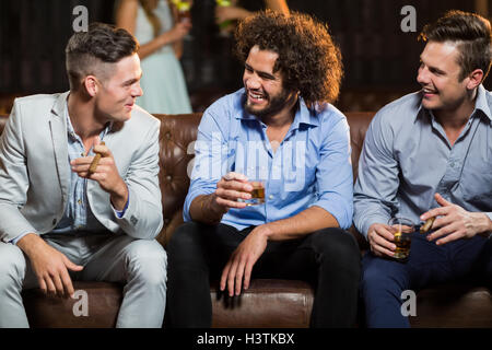 Les amis en interaction les uns avec les autres tout en ayant un cigare et whisky en bar Banque D'Images