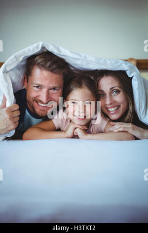 Famille heureuse allongé sous une couverture sur le lit Banque D'Images