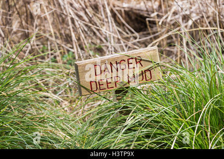 Panneau en bois rectangulaire avec écriture rouge en sol marécageux, boue Danger Banque D'Images