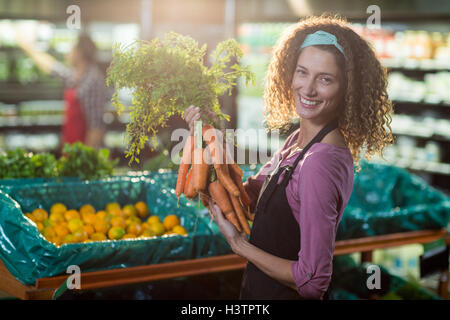 Le personnel féminin Smiling holding bunch de carottes dans la section bio Banque D'Images